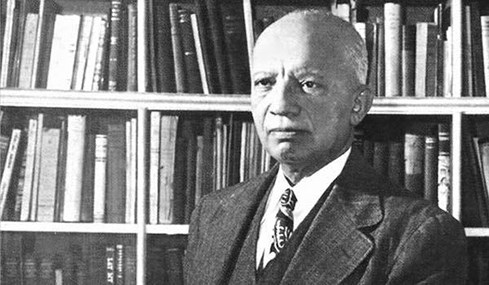 Historic photo of an older black man in a suit sitting in front of a bookshelf