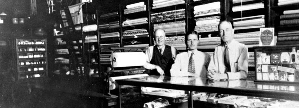 Historic image of three men behind a store counter with a variety of products for sale