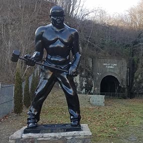A black metal statue of a strong man holding a hammer sits in front of a tunnel
