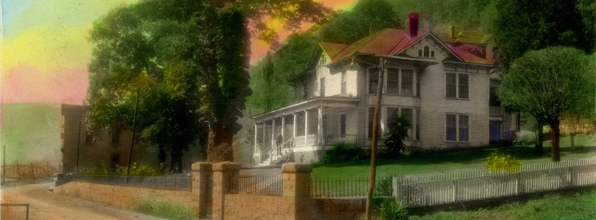 A large, fancy white house with a red roof sitting on a hill with a stone and white fence around it.