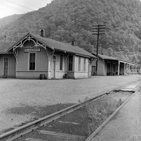 A yellow wooden train station with a sign that says Quinnimont on it sitting next to old railroad tracks