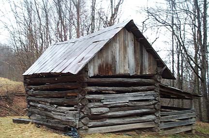 An old log barn sitting in a brown field
