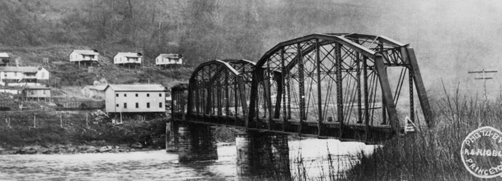 historic photo of bridge crossing a river with houses on the other side