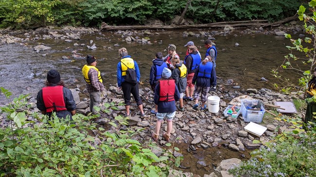 Ranger with 10 kids in lifejackets near a stream.