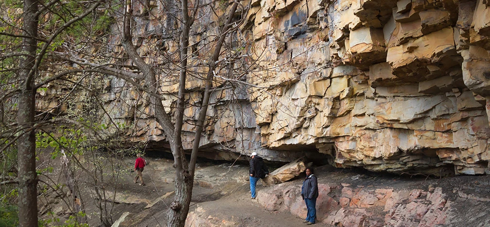 Hikers on a trail along the base of a cliff Hikers on a trail along the base of a cliff