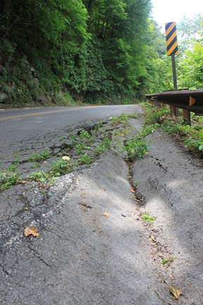 road with damaged area crumbling off side into woods road with damaged area crumbling off side into woods