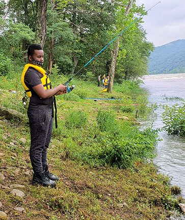 teen wearing mask and life jacket fishing in river