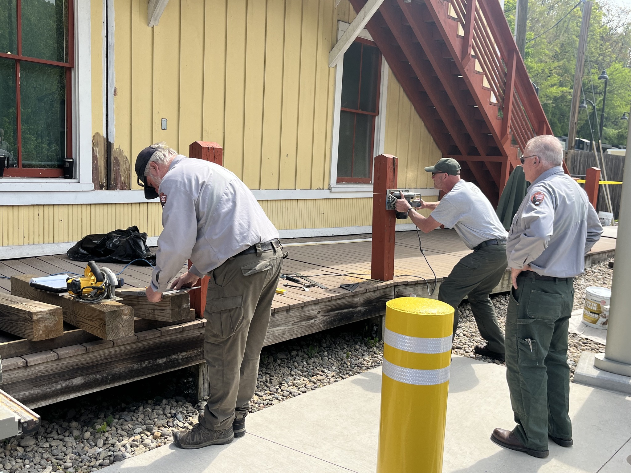 Three rangers in front of historic train depot working on fixing wooden posts using power tools