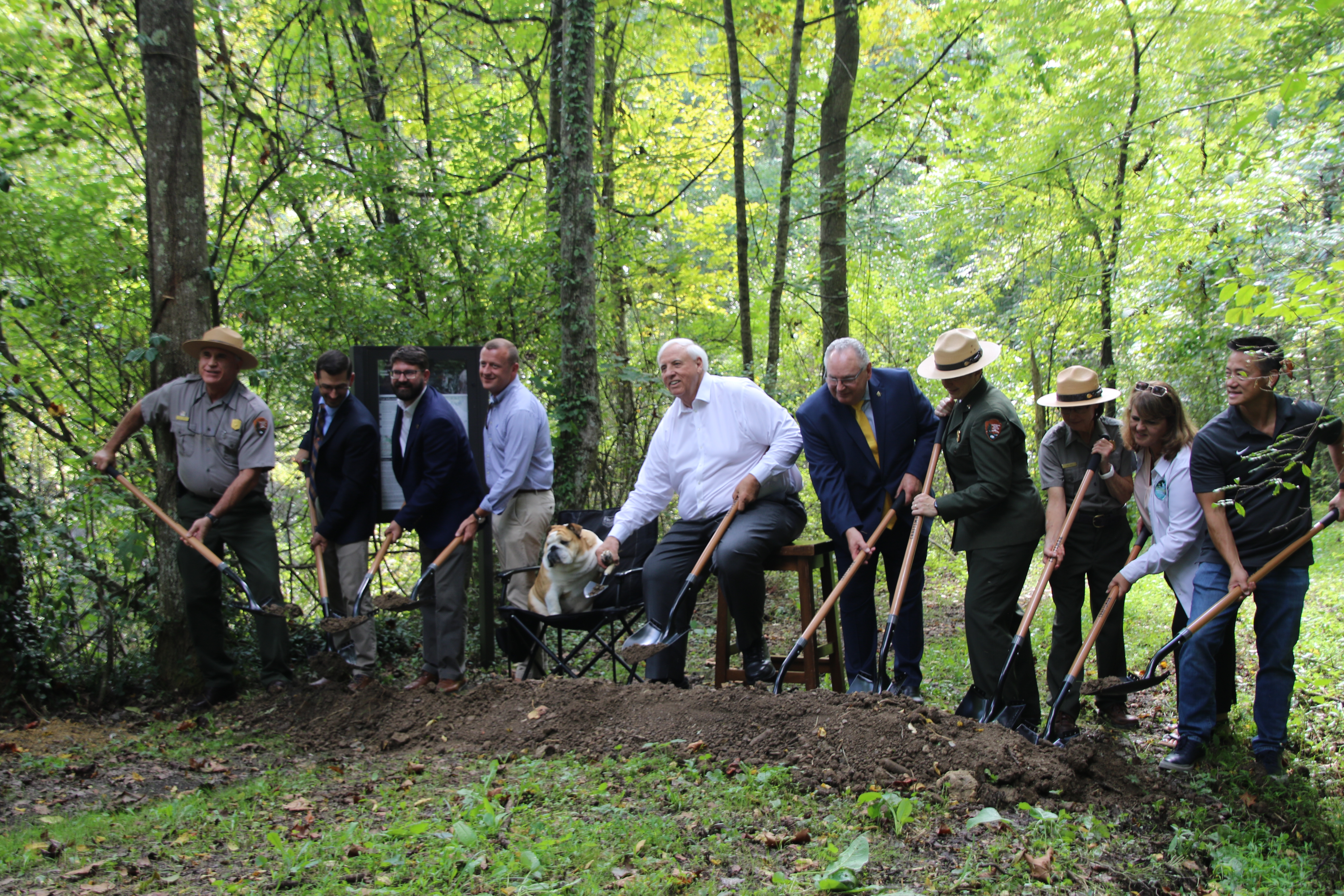 a line of people tossing dirt from shovels at a trailhead