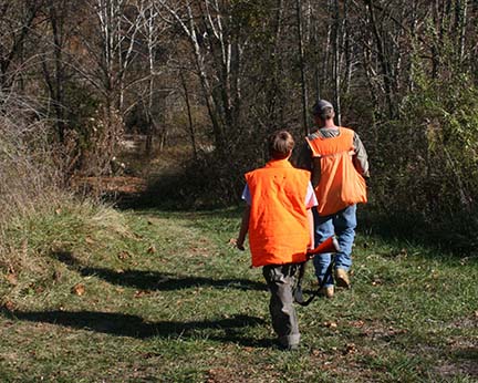 father and son wearing orange camo walking down trail