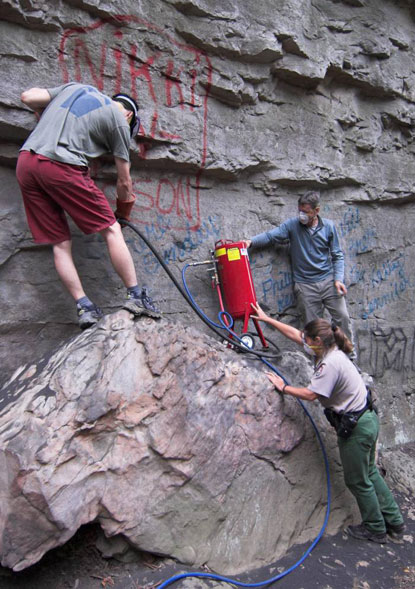 Volunteers and park ranger cleaning graffitti off of rock cliff