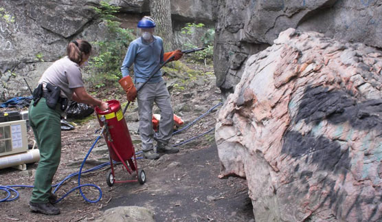 Ranger and volunteer sandblasing graffitti off of rock cliff.