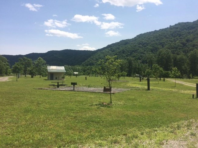 A grassy field with picnic tables, grills, and a restroom building in it