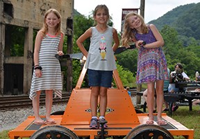 3 young girls are standing on a bright orange hand cart.