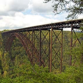 A large arched bridge spanning a gorge covered in bright green trees.
