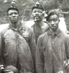 Black and white photo of three African America men dressed in coal miners helmets with lamps and long sleeve button down shirts