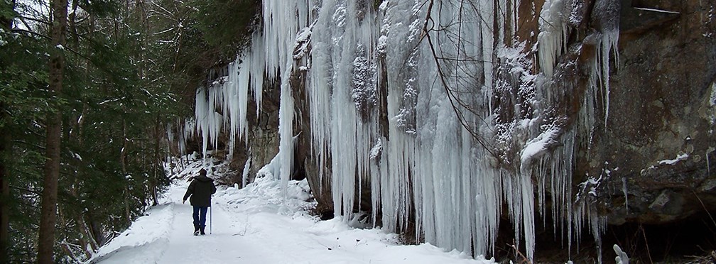 Hiker walking alongside frozen waterfall Hiker walking alongside frozen waterfall