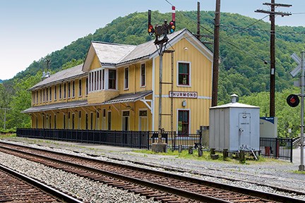 A yellow two story train depot with railroad tracks in front of it.