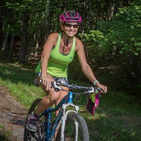 A colored photograph of a woman wearing a helmet, riding her bike on the trail.