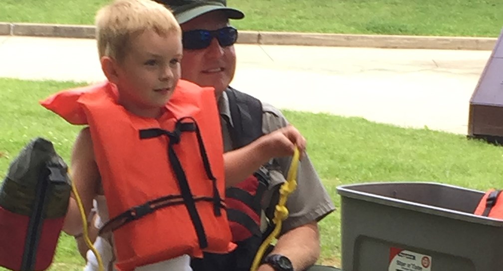 a young boy in a life jacket practices using a throw rope