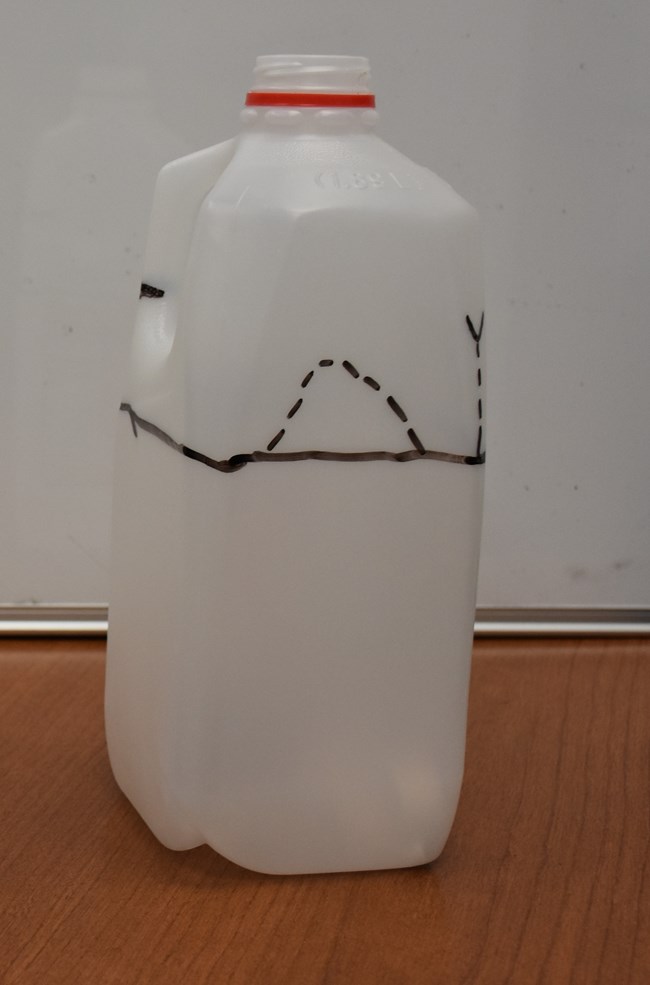 An empty half-gallon milk-jug with lines drawn on it.