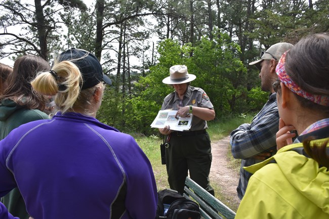 Ranger wearing flat hat is pointing to a series of pictures while standing in front of a group of people.