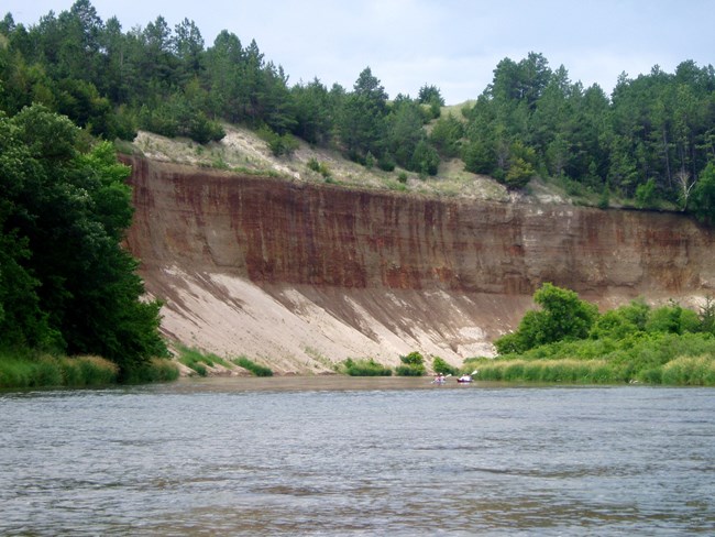 water seeps out of a red wall of exposed soil on a river bluff