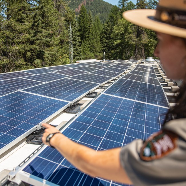 A ranger points at a solar array, with trees in the background