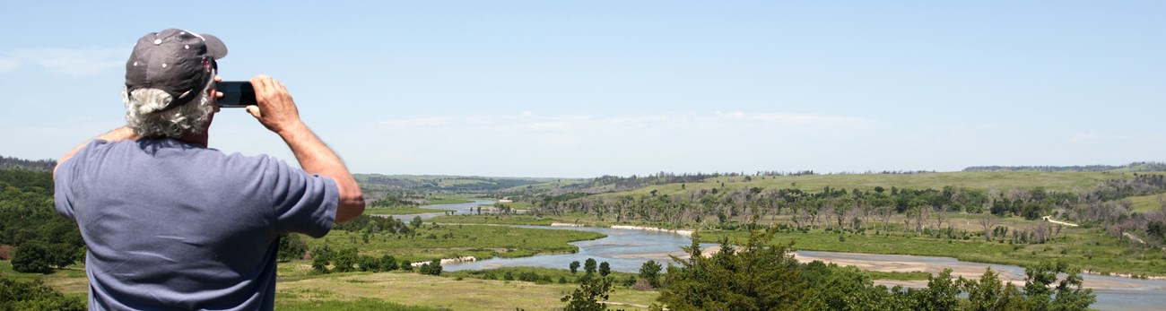 A person in a baseball cap takes a picture of the river's scenery