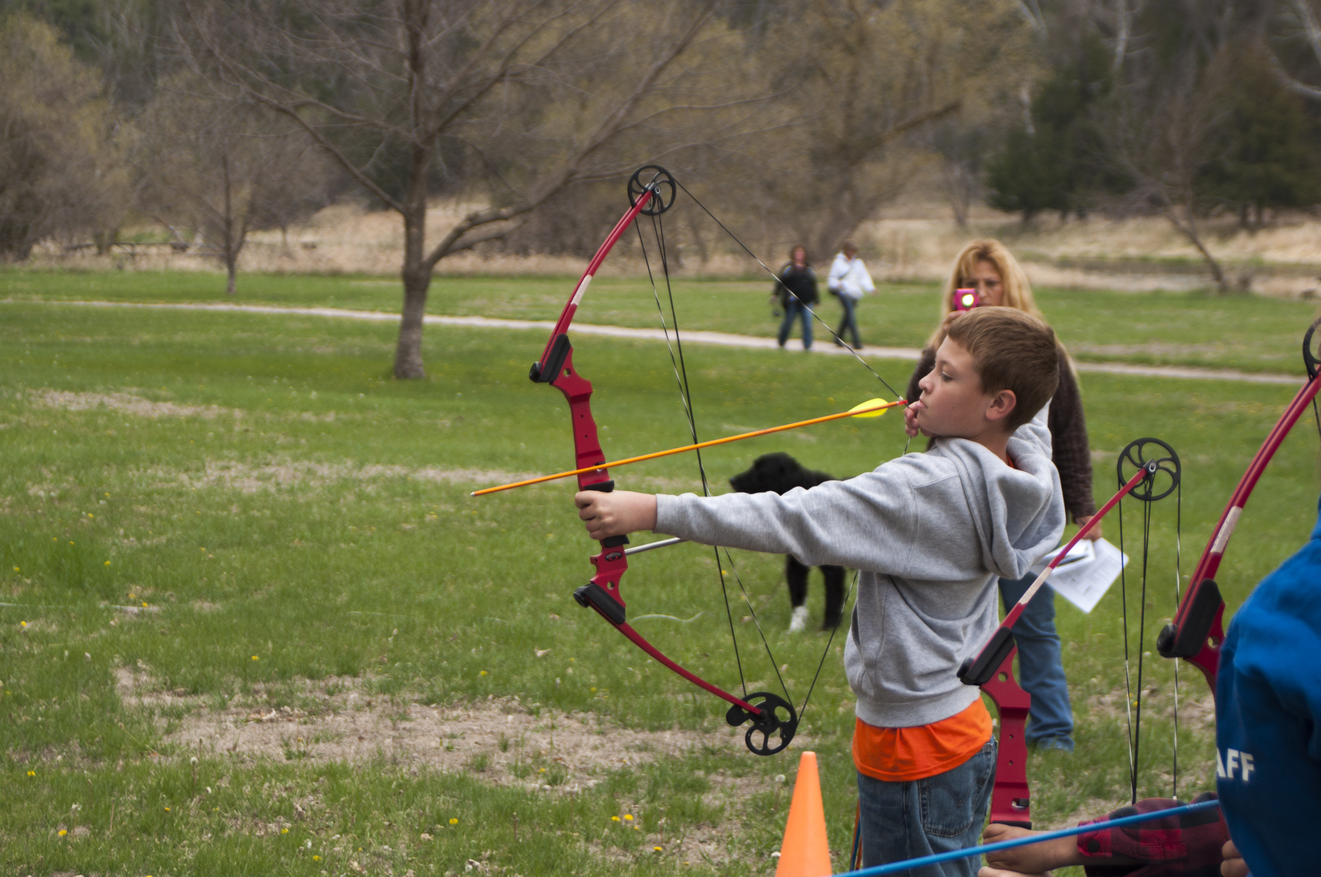 A boy lifts a bow to aim an arrow at a target at the Archery station.