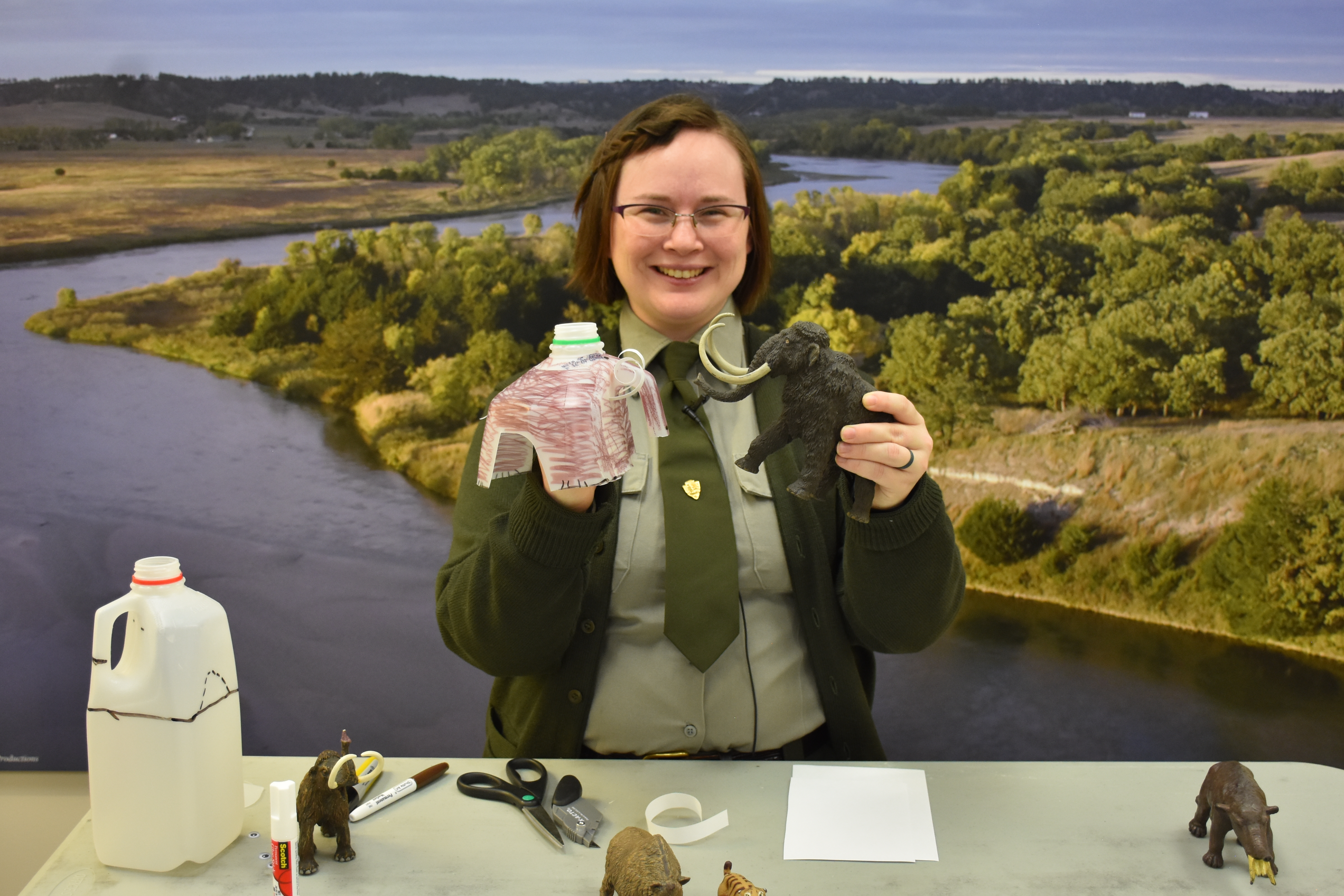 Ranger stands at table with milk carton craft and plastic mammoth.