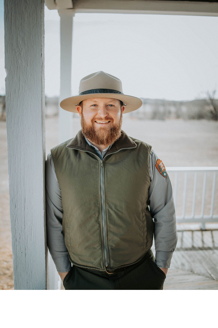 Photo of new superintendent Chris Mather wearing a National Park Service uniform standing on a white porch and smiling for the camera
