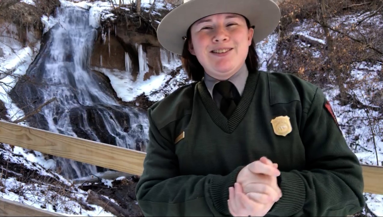 Bobbie and Fort Falls A ranger stands in front of a waterfall in winter.