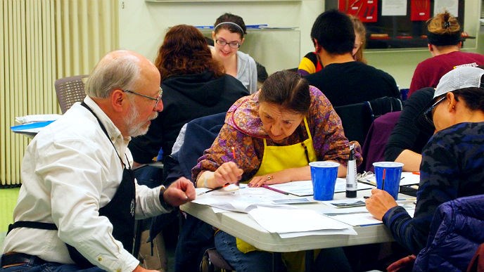 Kneeling man helps a woman with an art project