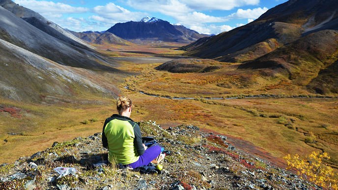 Woman sits on a rock and looks out at a mountain-ringed valley
