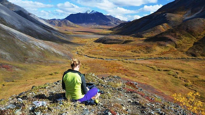 MK McNaughton and her view of Copter Peak Woman sits on a rock and looks out at a mountain-ringed valley