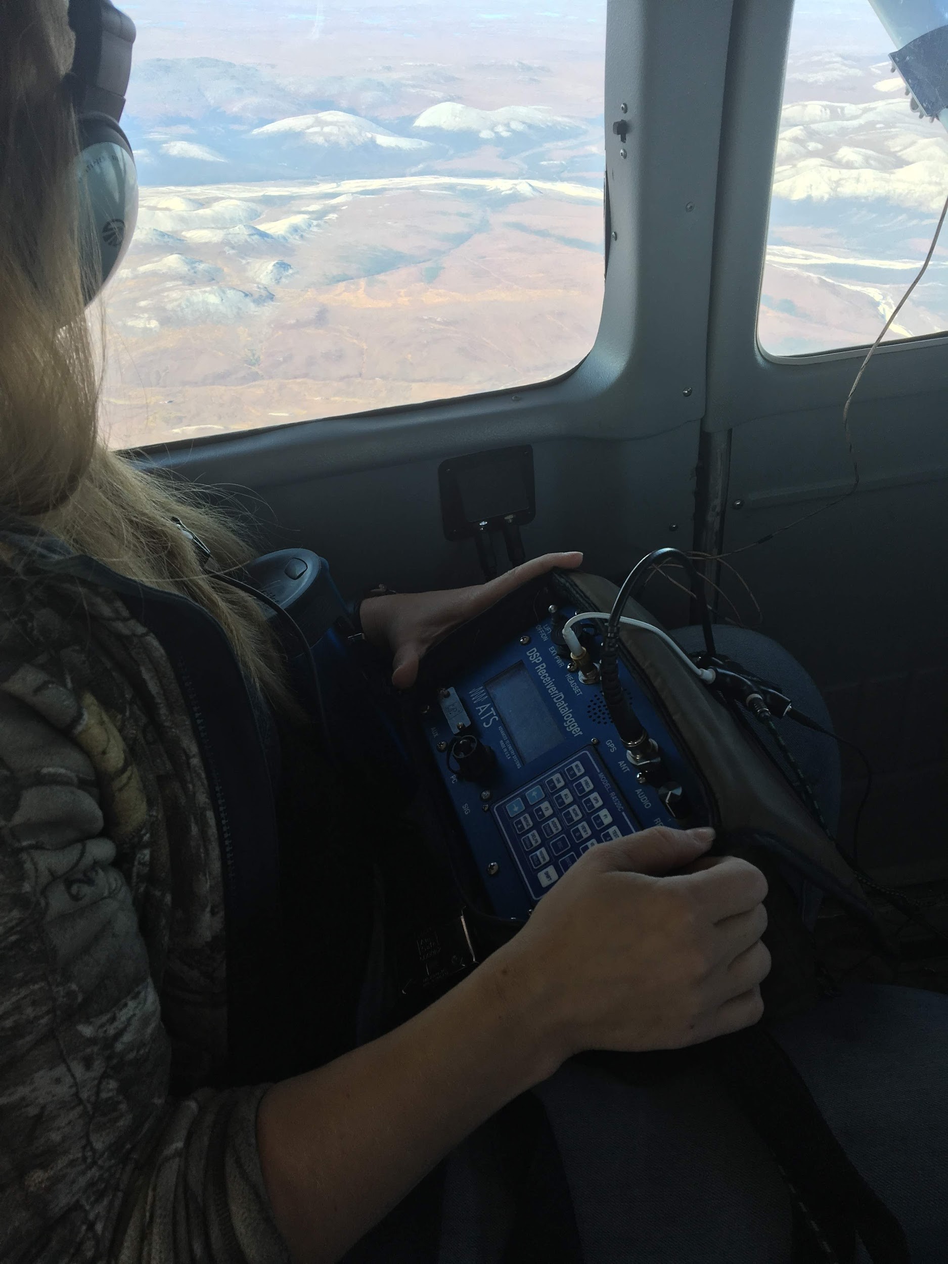 Girl using telemetry equipment and staring out the plane window at the tundra below