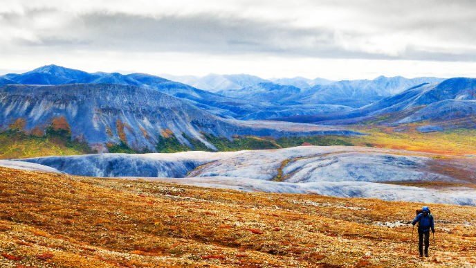 single person hiking on tundra with mountains behind