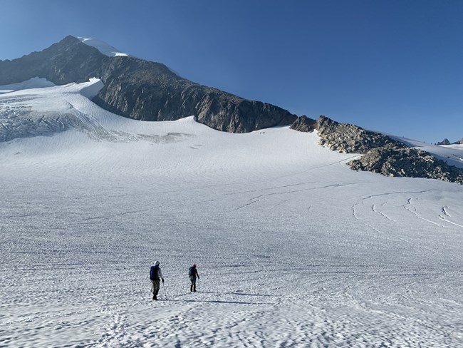 Mountain climbers walking on glacier with mountains in the background