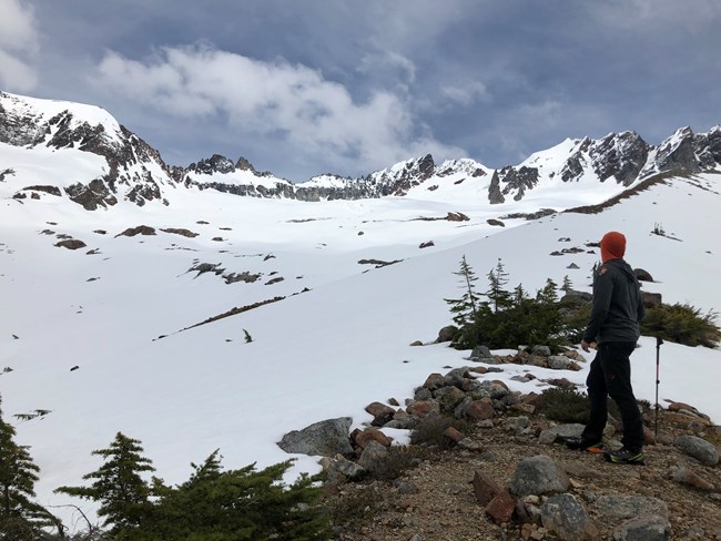 Ranger in foreground looks at a snowy Boston Basin mountain landscape.