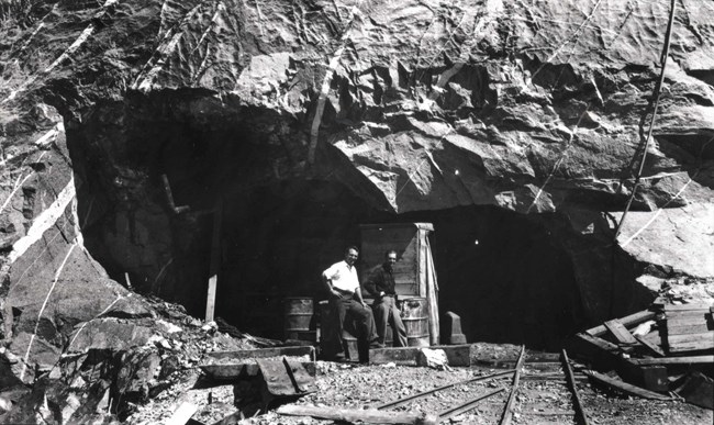 Two men stand outside a mine entrance.