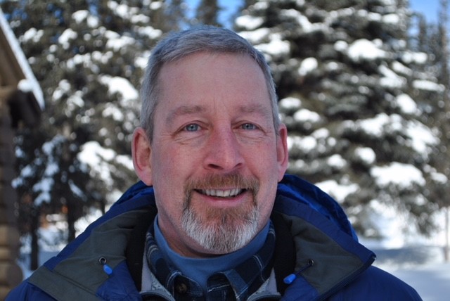 A portrait of Superintendent Don Striker, standing in front of snow-covered trees