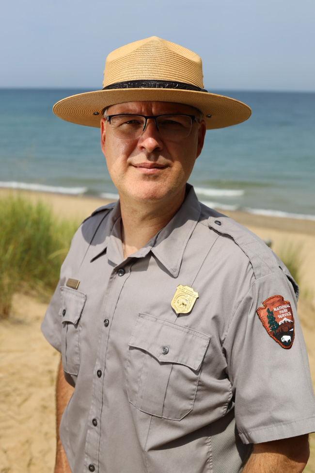 Man wearing ranger uniform and hat standing on a sandy beach