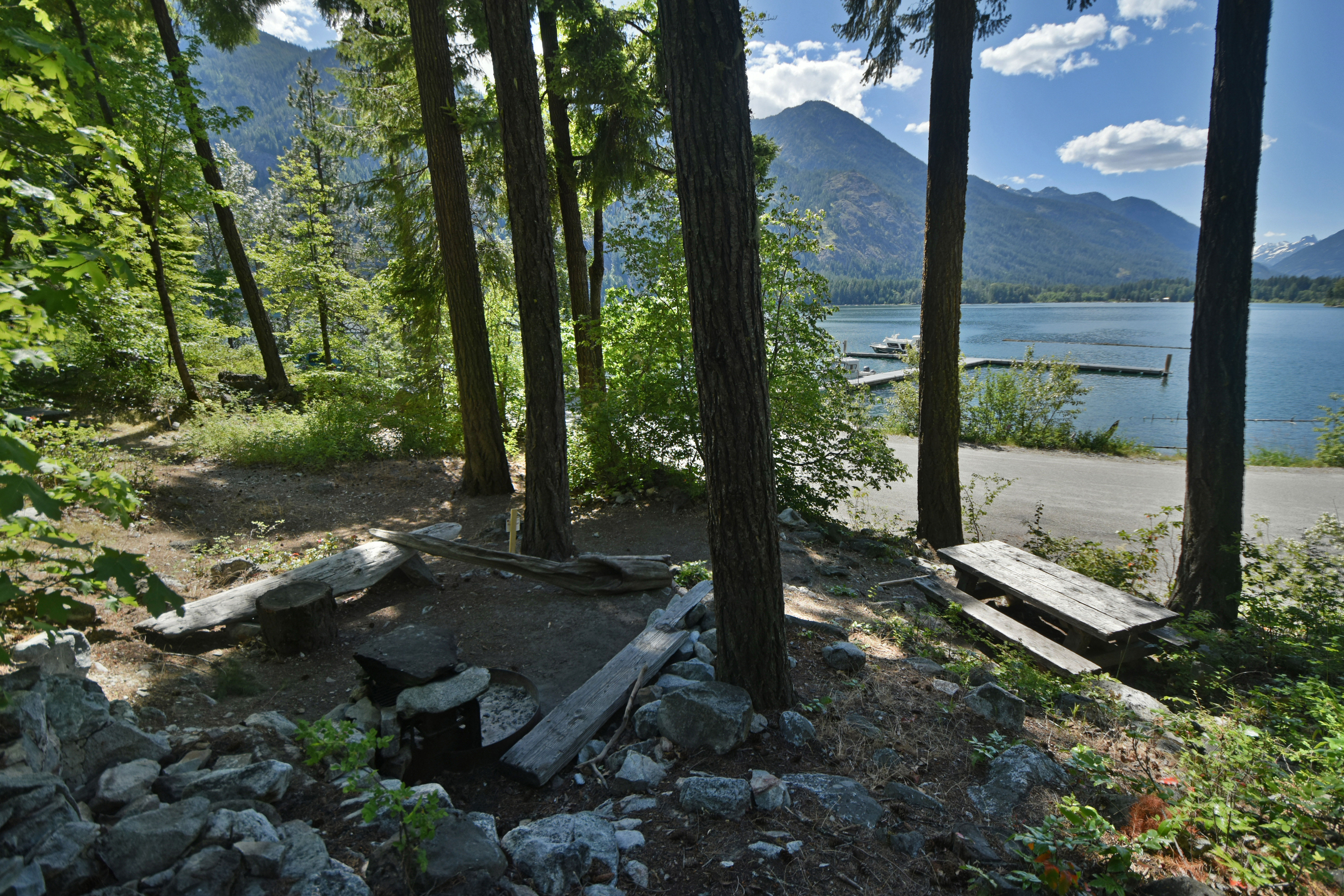 Looking over a campsite near the water with a tent pad and picnic table in the foreground and a lake in the background.