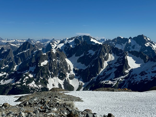 Rocky campsites in between large snow patches with a mountain view