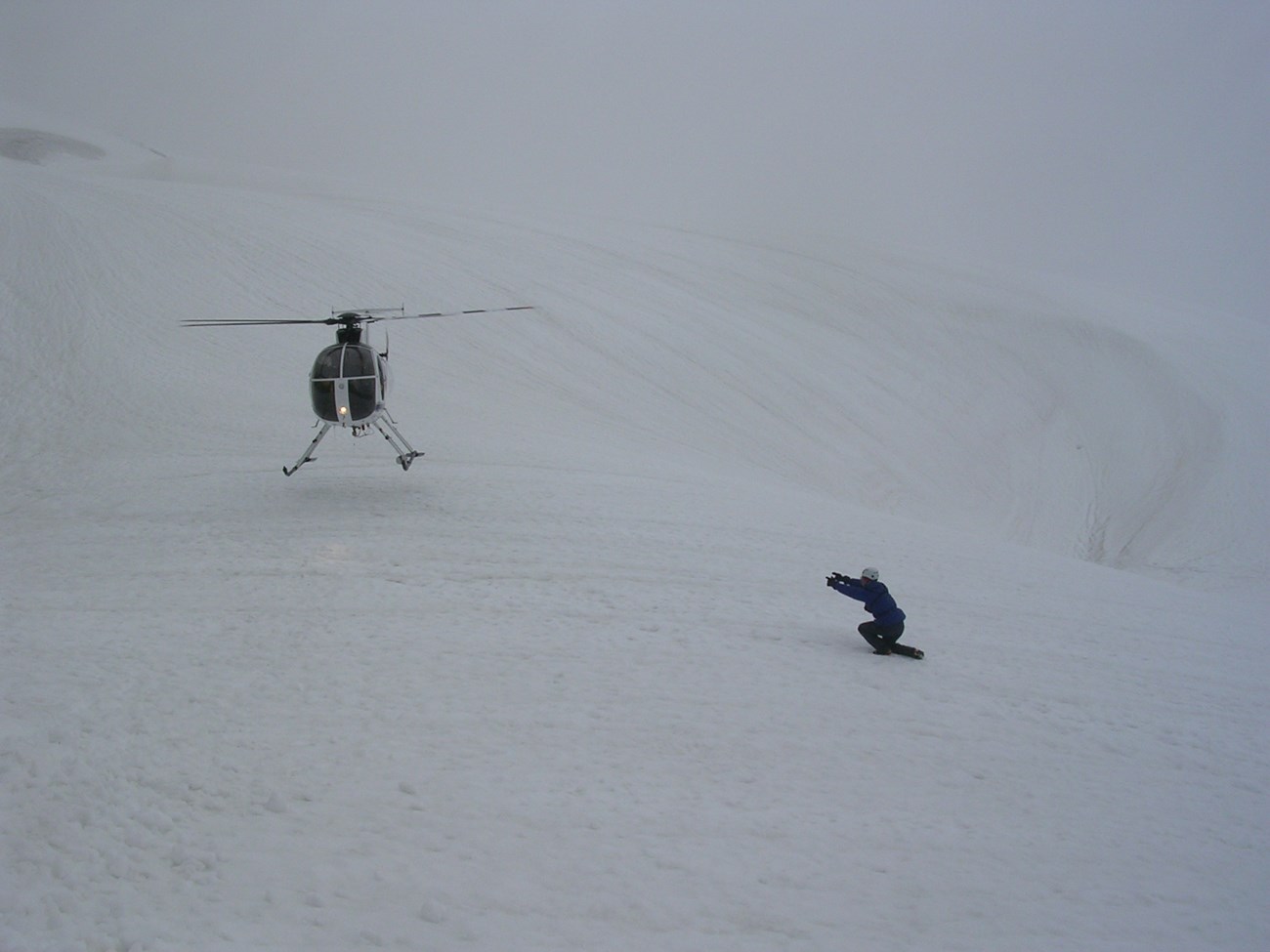Helicopter landing in fog on glacier with person directing the landing