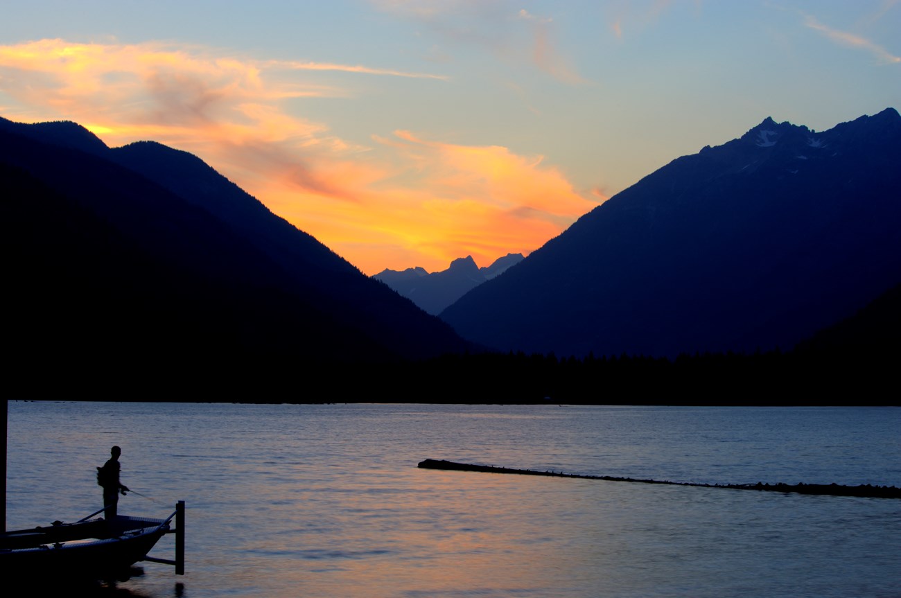 An angler silhouetted against a lake at sunset.