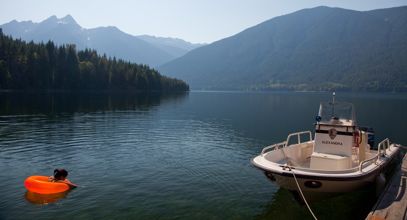 A person floating in the lake next to a docked boat.