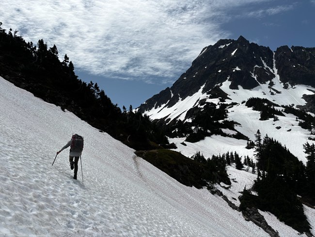 Hiker crossing steep snow near Cascade Pass.