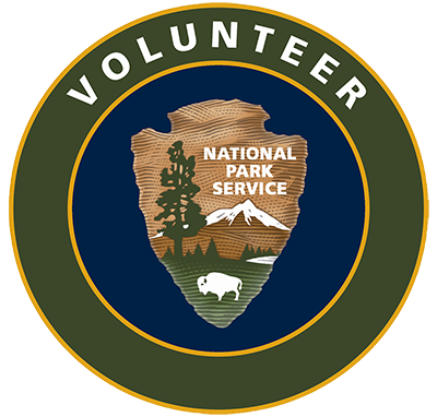 National Park Service Arrowhead on a field of blue with a green circle around it. Text in the green circle reads "Volunteer."